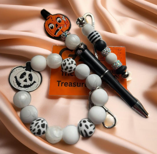 “Handmade Halloween gift set by Galaxy Artwork featuring a beaded pen, keyring bracelet, and bookmark with pumpkin and ghost charms in black, white, and orange tones.
