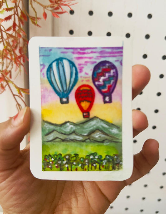 Hand-painted ACEO card with colorful hot air balloons above mountains at sunrise.