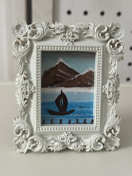 Decorative white frame with a small painting of a sailboat on water.