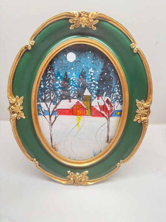 Mini acrylic painting of a red winter cabin with snow-covered trees and a full moon in a decorative green and gold oval frame.