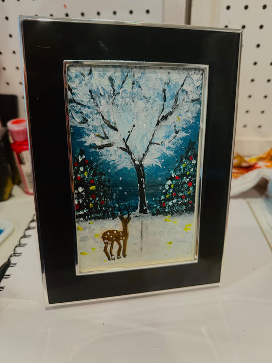 Framed artwork of a deer in a snowy landscape with trees and colorful lights. Handmade art.