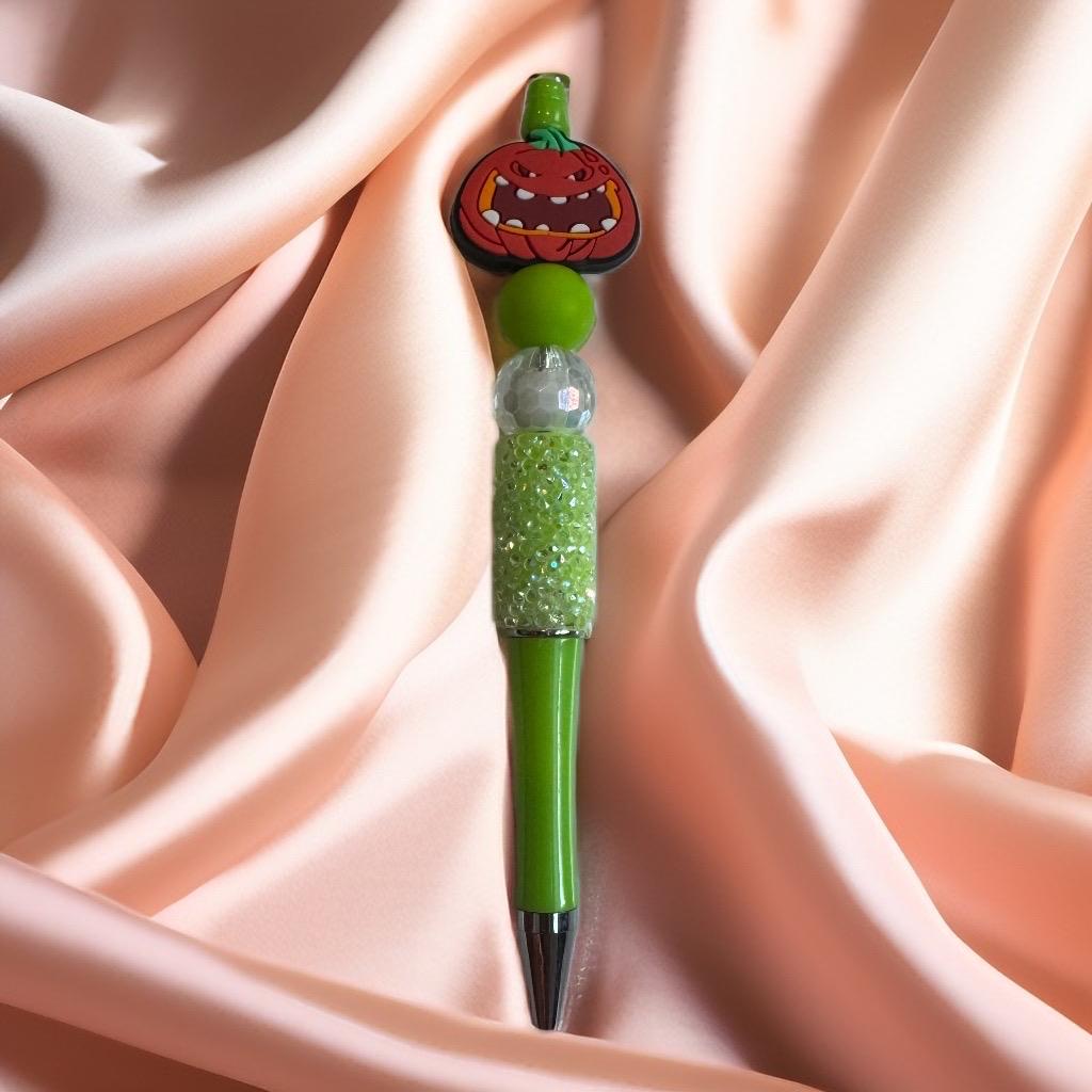 Green beaded pen featuring grinning pumpkin face and crystal beads, handmade Halloween stationery.