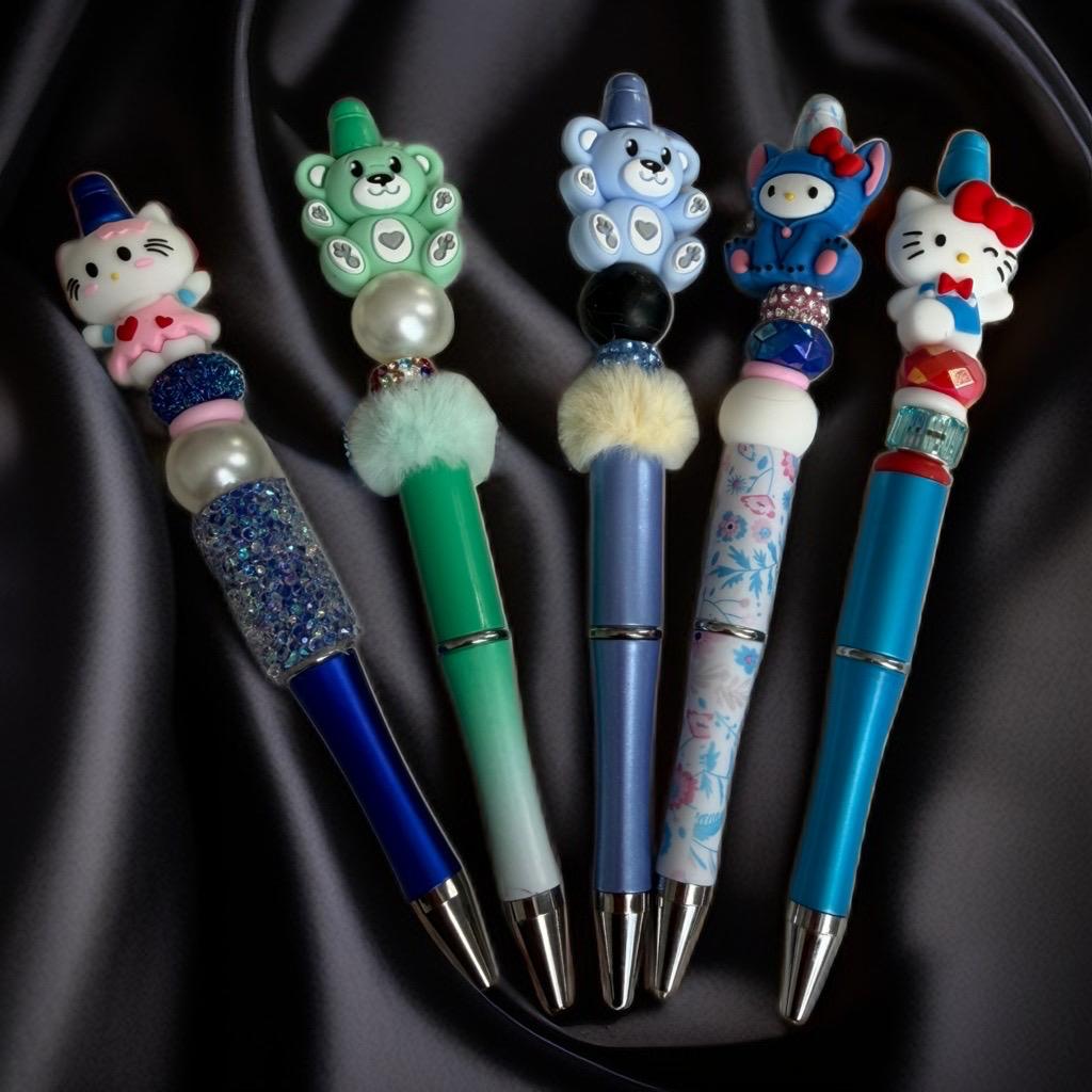 Handmade beaded pens with cute animal character toppers in blue, green, and pink.