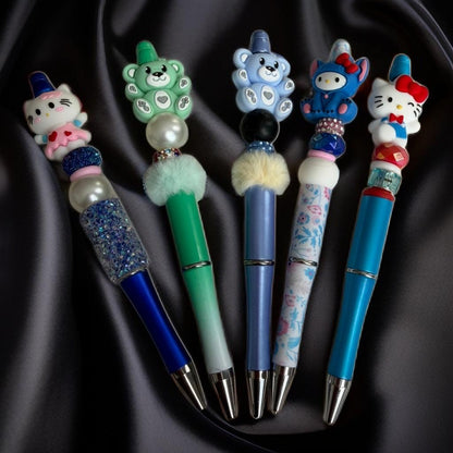 Handmade beaded pens with cute animal character toppers in blue, green, and pink.