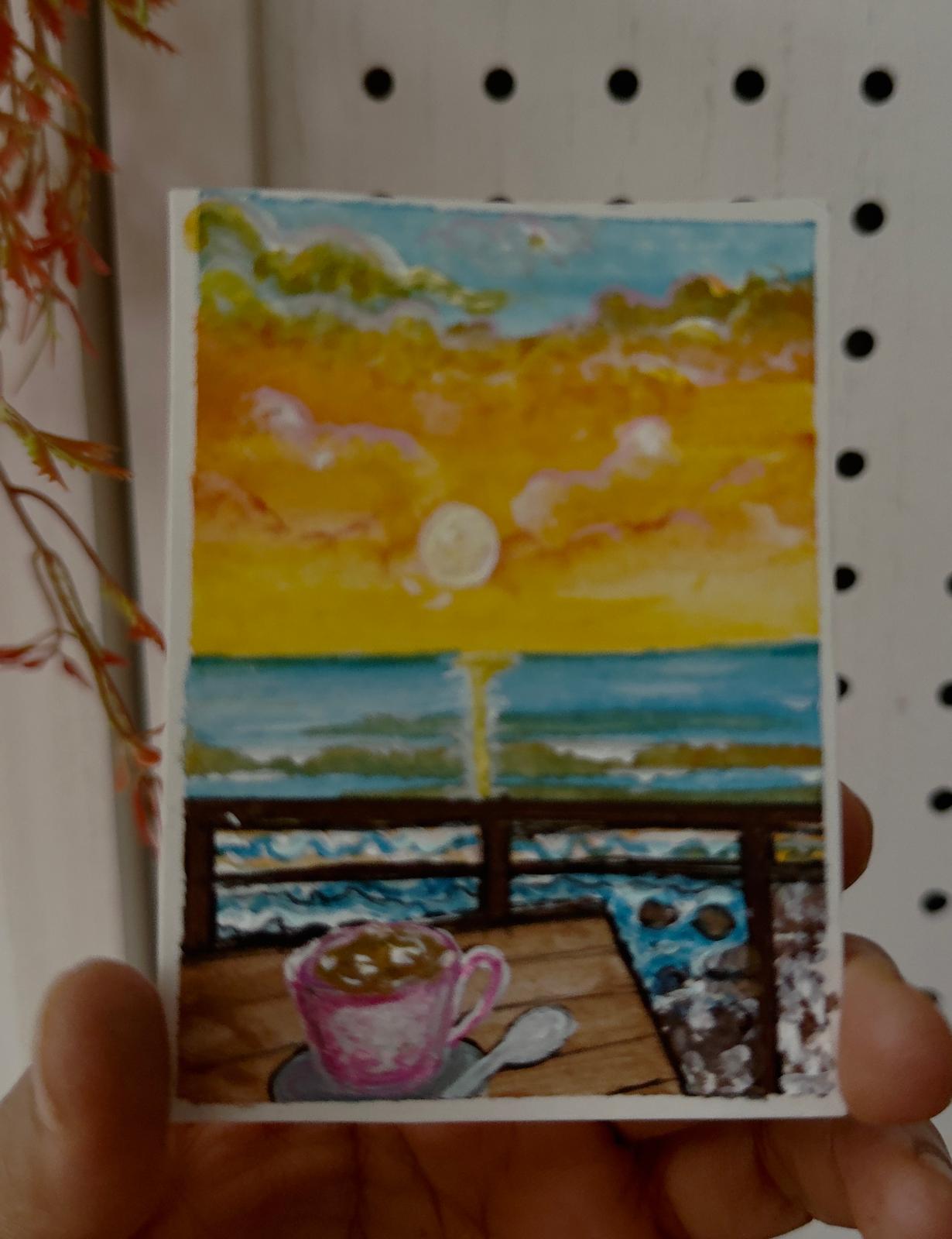 Hand-painted ACEO card of ocean sunset with waves and coffee cup on a deck.