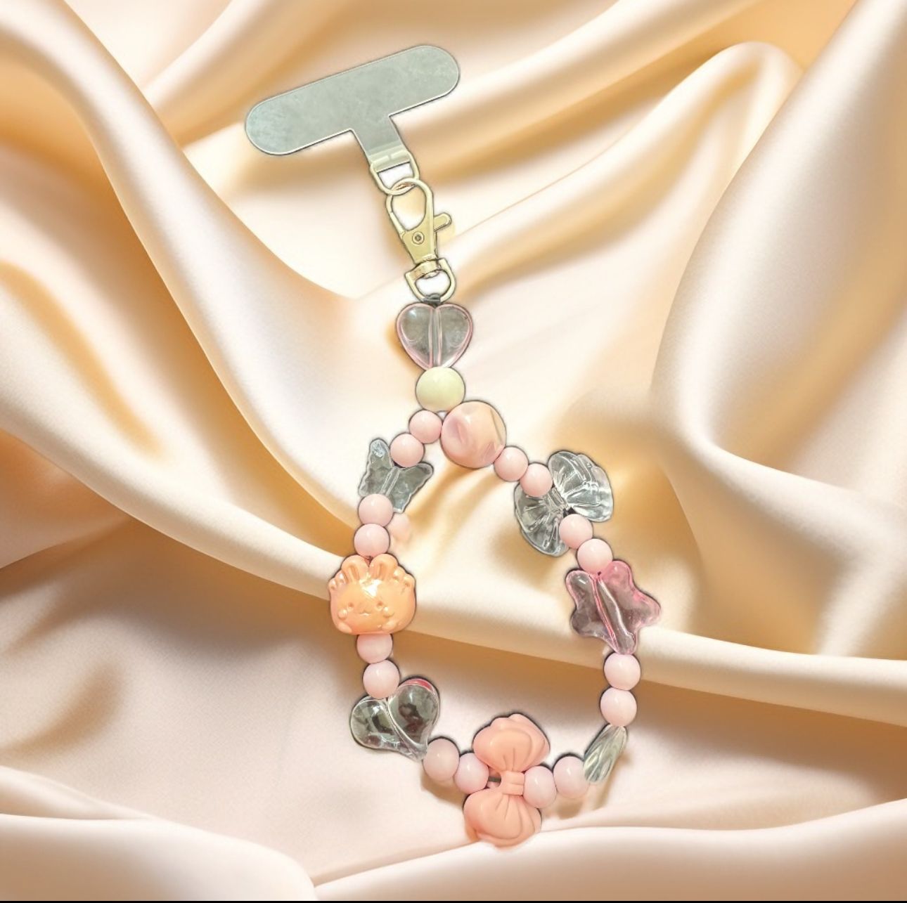 Handmade pastel beaded mobile phone charm with butterfly, heart, and bow beads in peach and clear tones with silver phone strap clip.