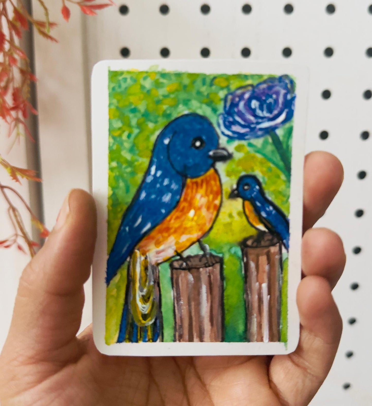 Hand holding a card with a colorful illustration of two birds on a pegboard background