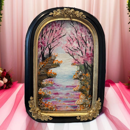Decorative wall art with cherry blossom trees and a path in a decorative frame on a pink background.