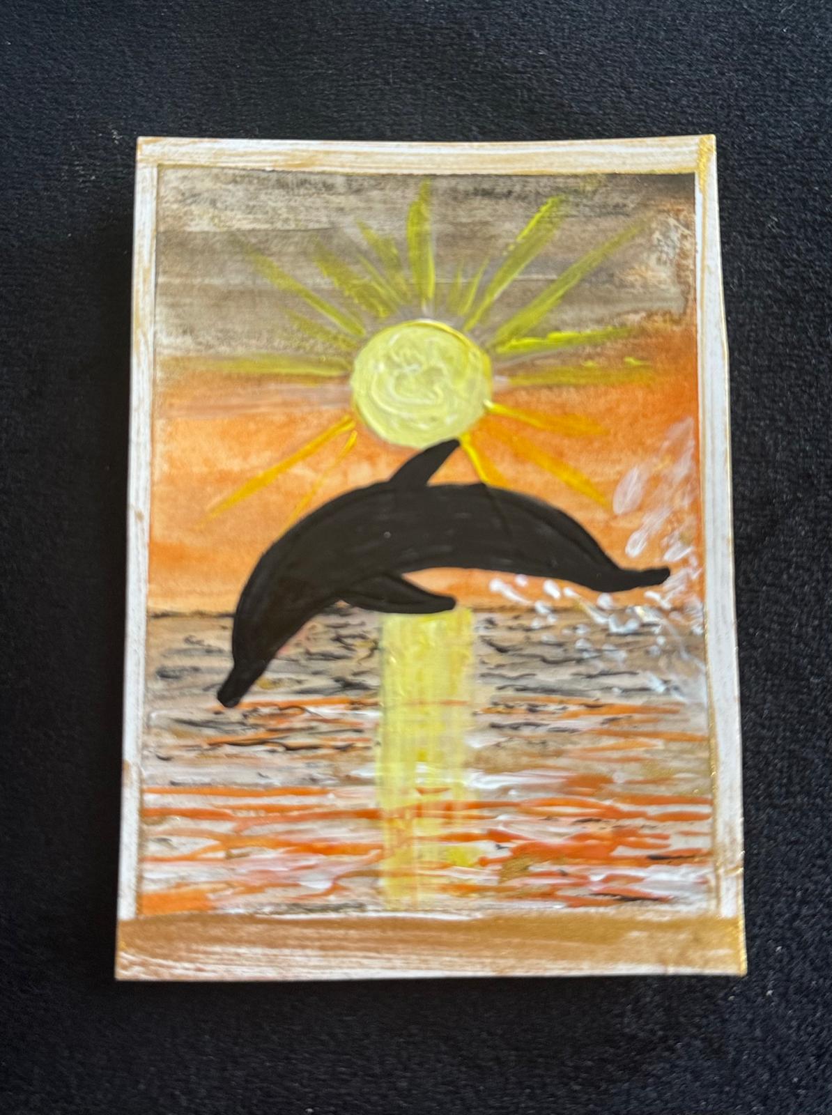 Silhouette of a dolphin leaping out of the ocean against a glowing orange and yellow sunset.
