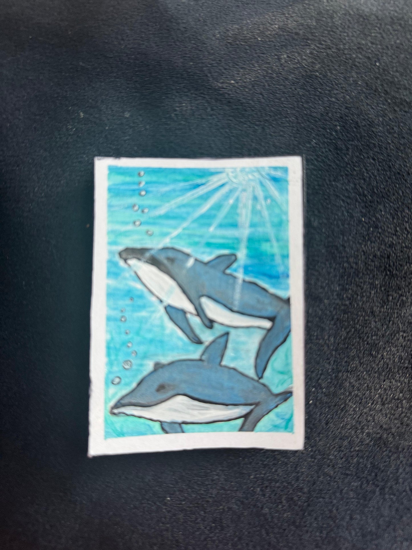 Two dolphins swimming underwater with bubbles and sunlight streaming through the ocean surface.