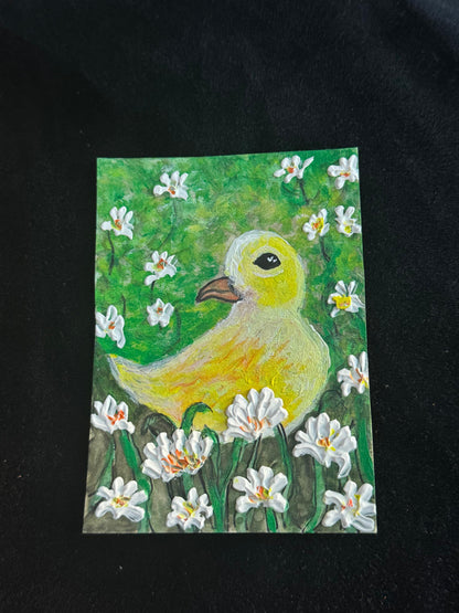 Handmade ACEO artwork of a yellow duck surrounded by white blooming flowers in a green meadow.
