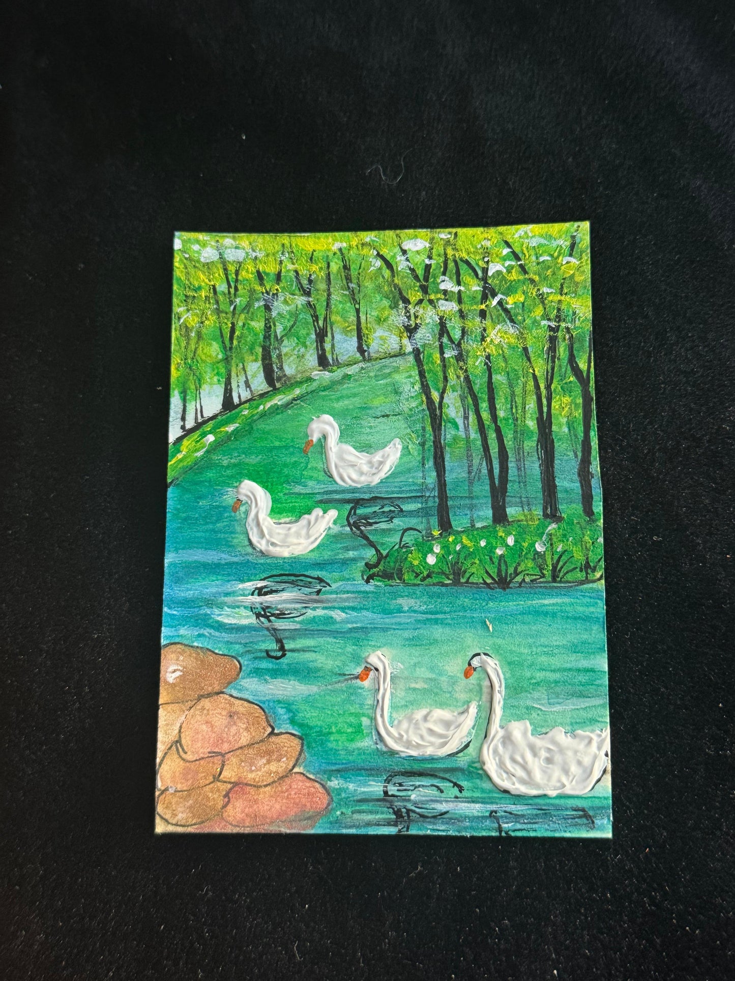 Miniature ACEO card of swans swimming peacefully in a green woodland landscape with trees and water reflections.
