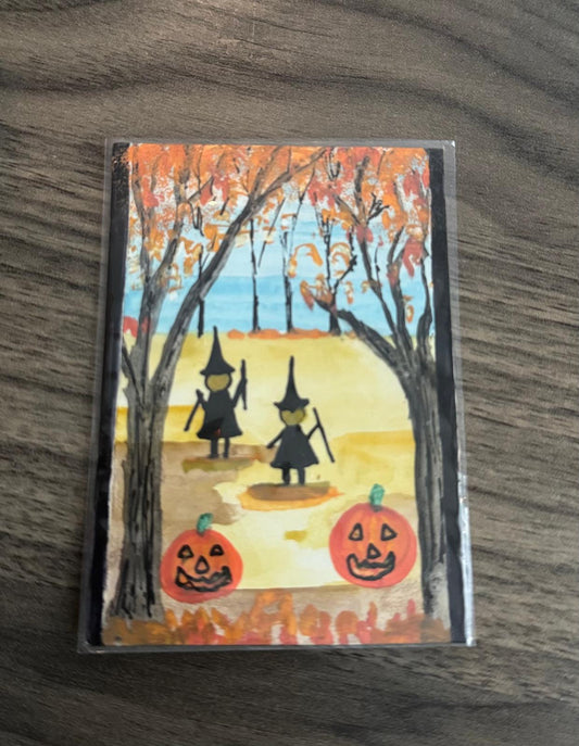 Halloween-themed card with two witches and pumpkins on a wooden surface