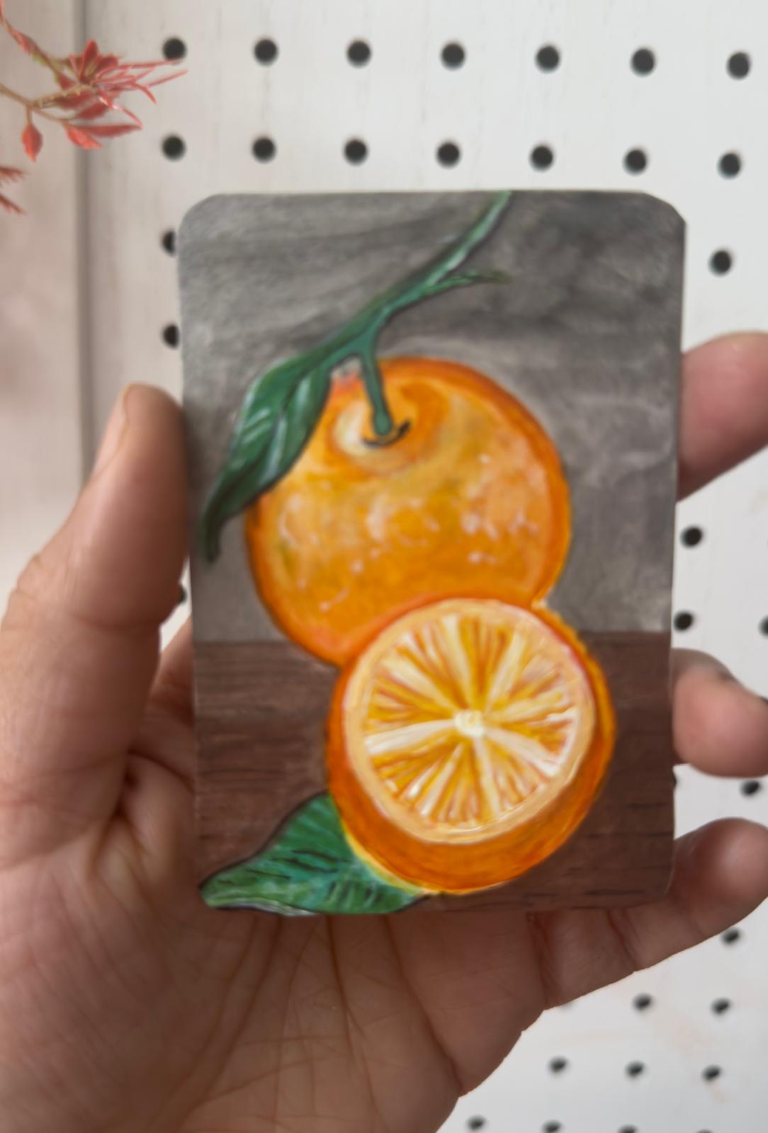 Hand-painted ACEO card of orange with slice and leaves on rustic table.