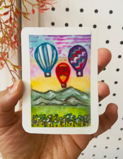 Hand-painted ACEO card with colorful hot air balloons above mountains at sunrise.