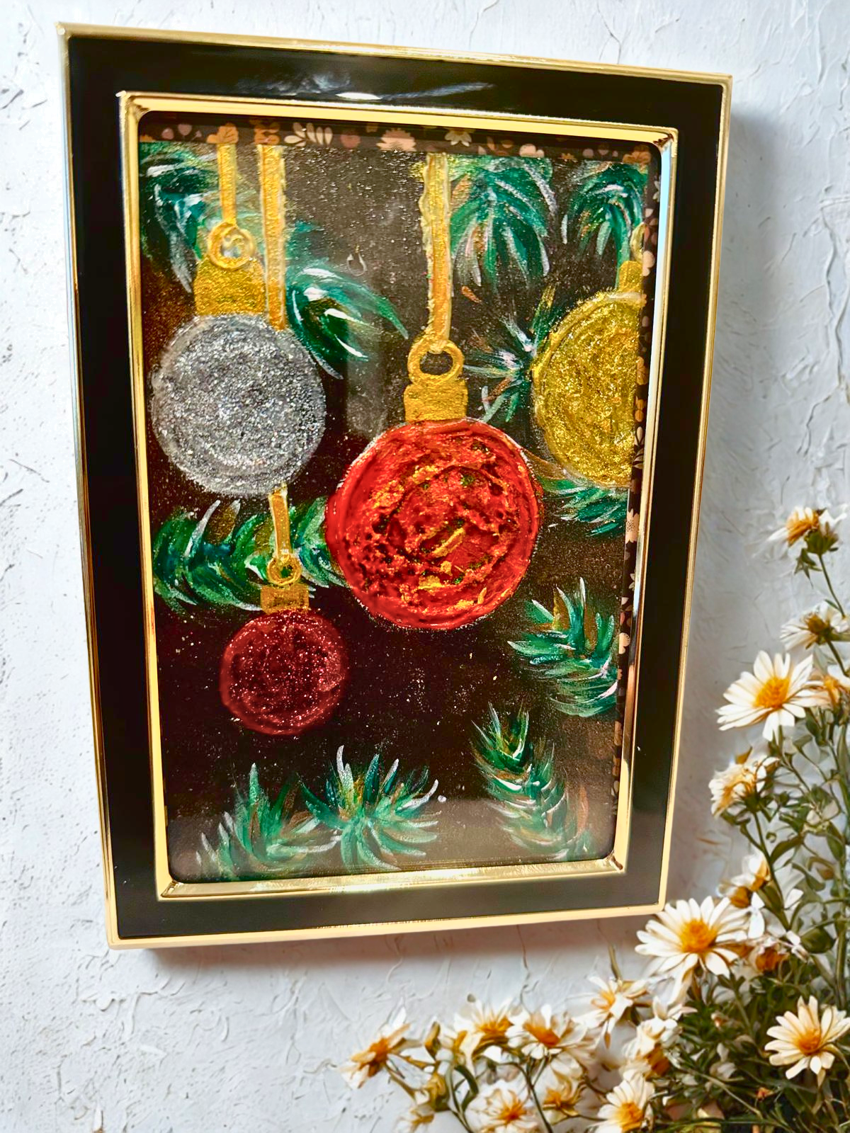 Decorative card with glittery Christmas ornaments on a textured surface with flowers.