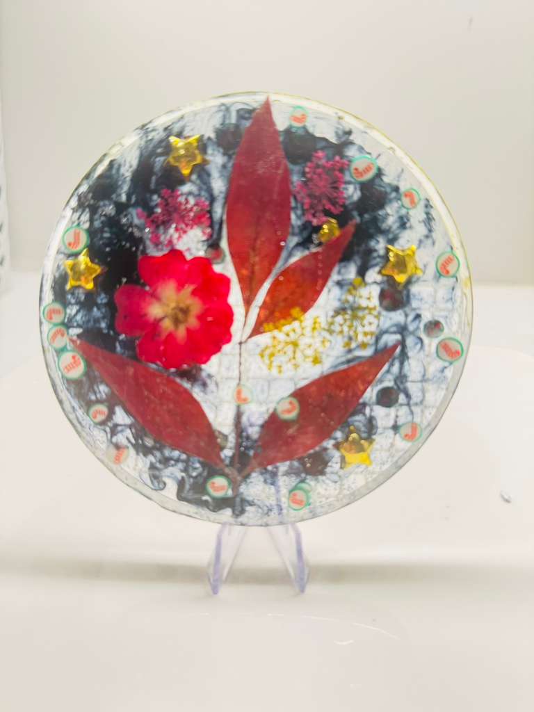 Handmade resin art coaster featuring red leaves, dried flowers, gold stars, and holiday glitter.
