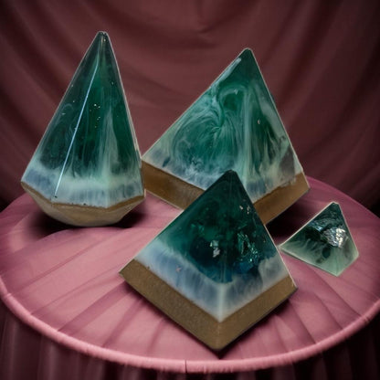 Pyramid-shaped decorative items with green and blue marbled design on a marble surface with roses.