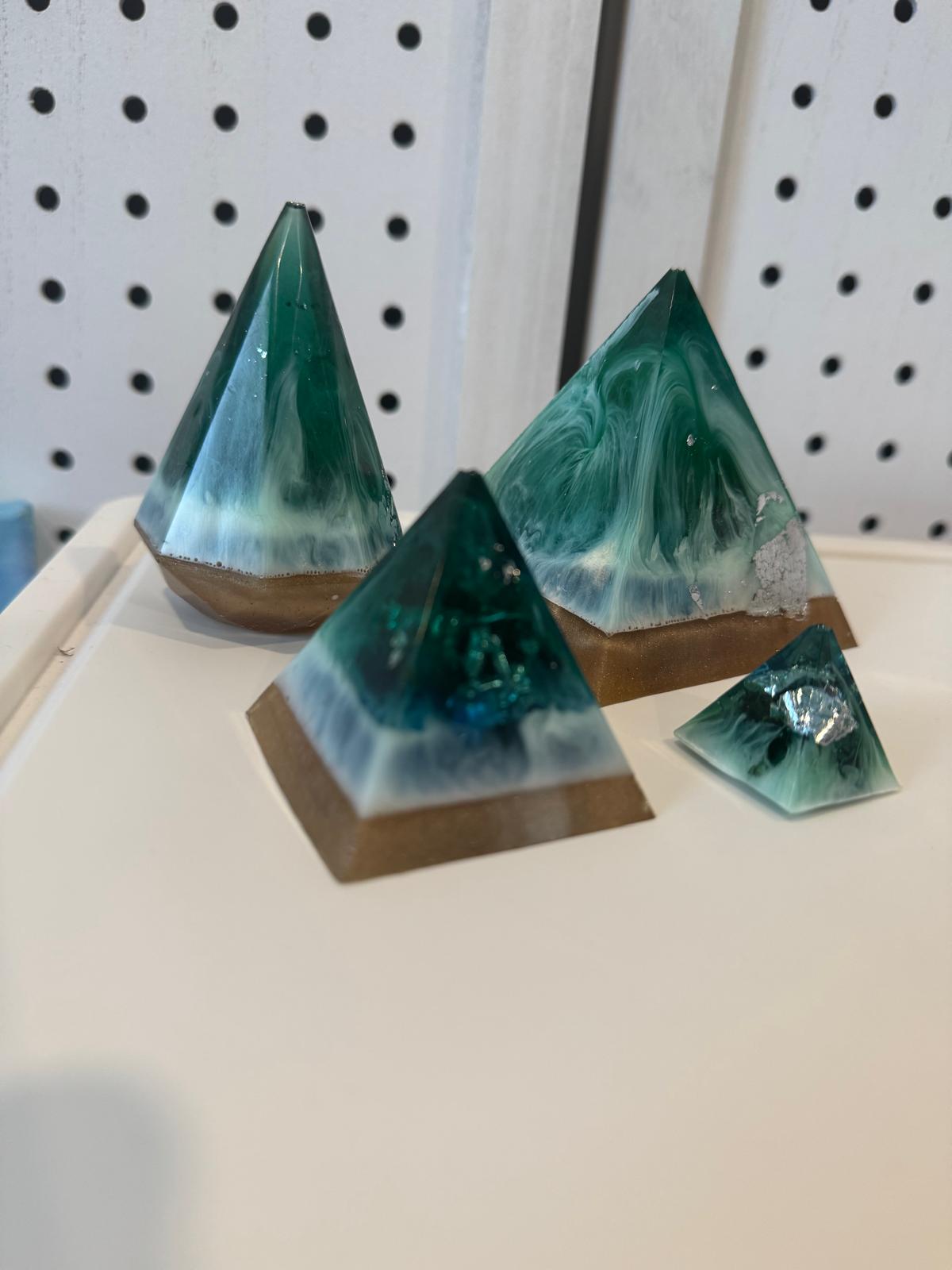 Pyramid-shaped green and brown resin sculptures on a white surface with a pegboard background.
