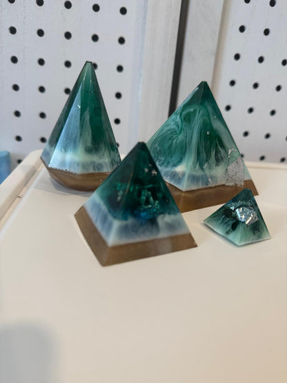 Pyramid-shaped green and brown resin sculptures on a white surface with a pegboard background.