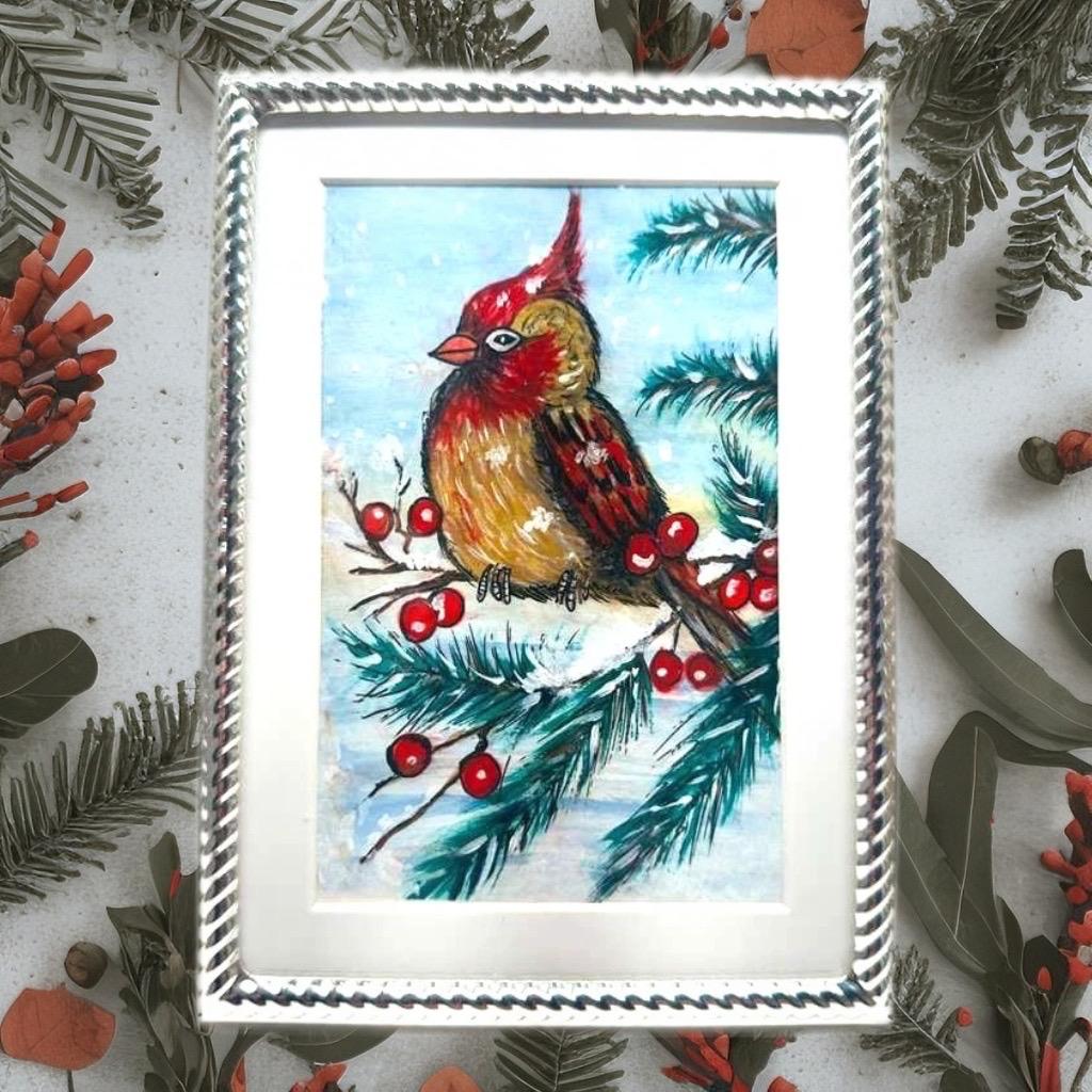 Original seasonal artwork of a cardinal bird in snow, displayed in a textured silver frame for holiday home décor.