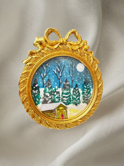 Handmade mini acrylic painting of a snowy winter cabin with pine trees and a full moon in a round gold ornament frame.