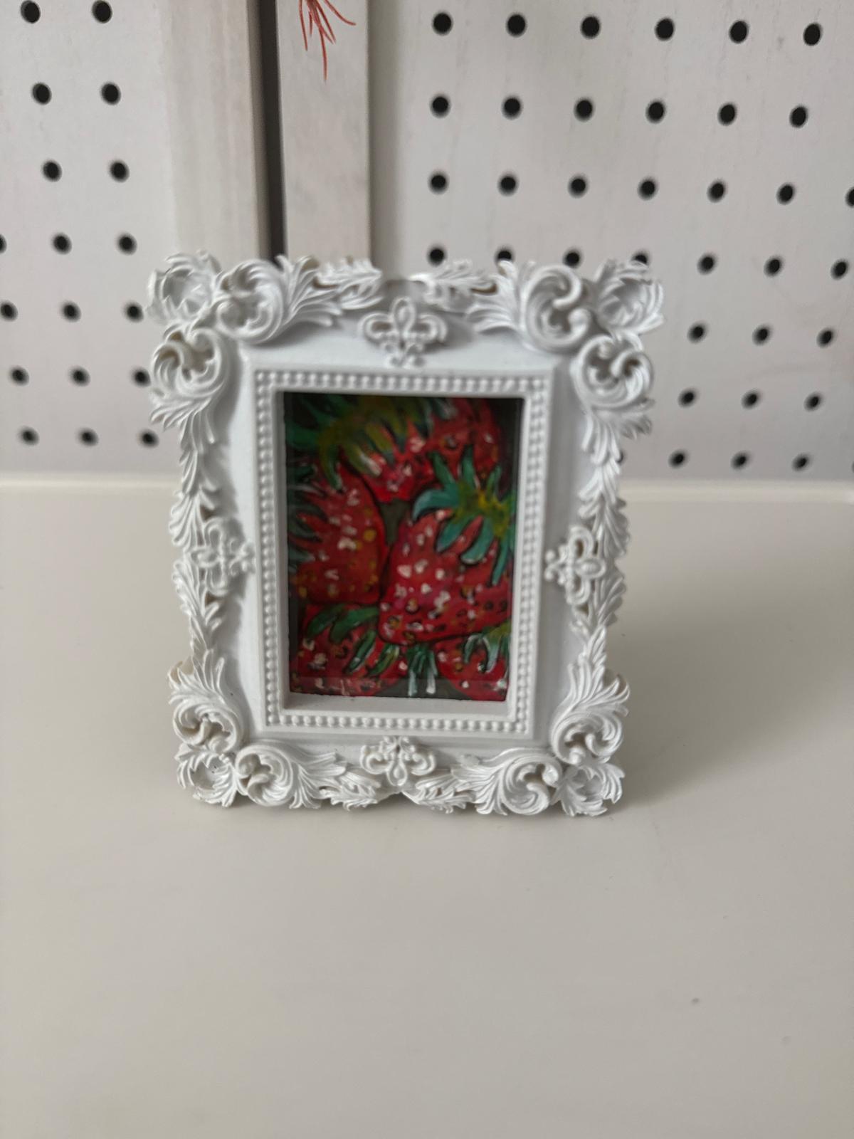 Decorative white frame with a colorful painting inside, against a pegboard background.