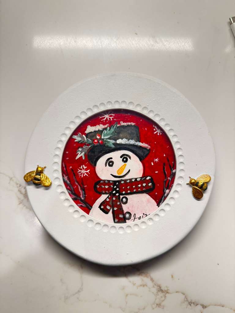 Handmade acrylic mini painting of a snowman in a winter scene on a round white frame with gold bee accents.