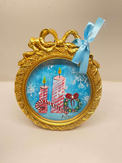 Handmade mini acrylic painting of two striped candles, a wreath, and a candy cane in a round gold frame with a blue ribbon.