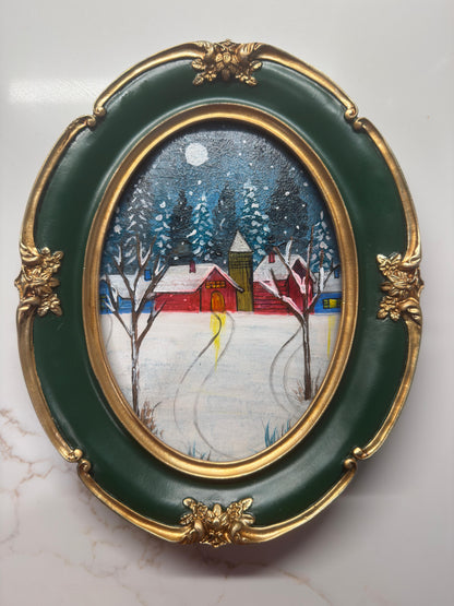Mini acrylic painting of a red winter cabin with snow-covered trees and a full moon in a decorative green and gold oval frame.