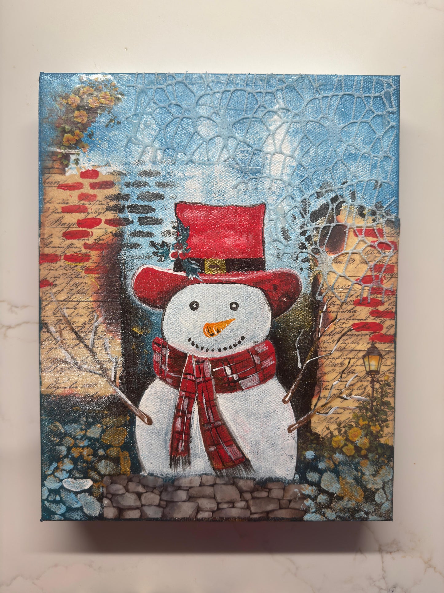 Handmade acrylic painting of a snowman wearing a red hat and scarf with a textured winter brick background.
