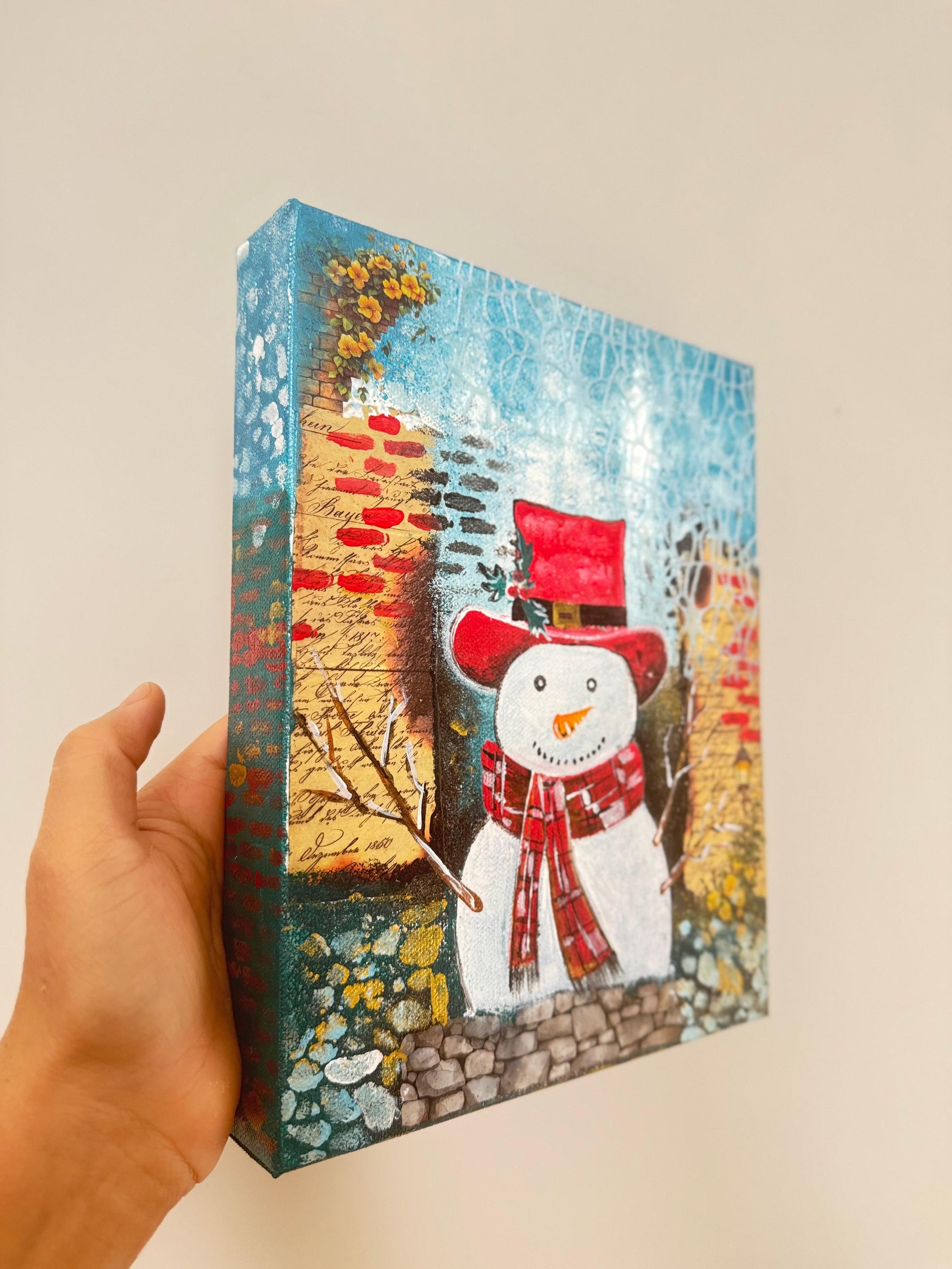 Handmade acrylic painting of a snowman wearing a red hat and scarf with a textured winter brick background.