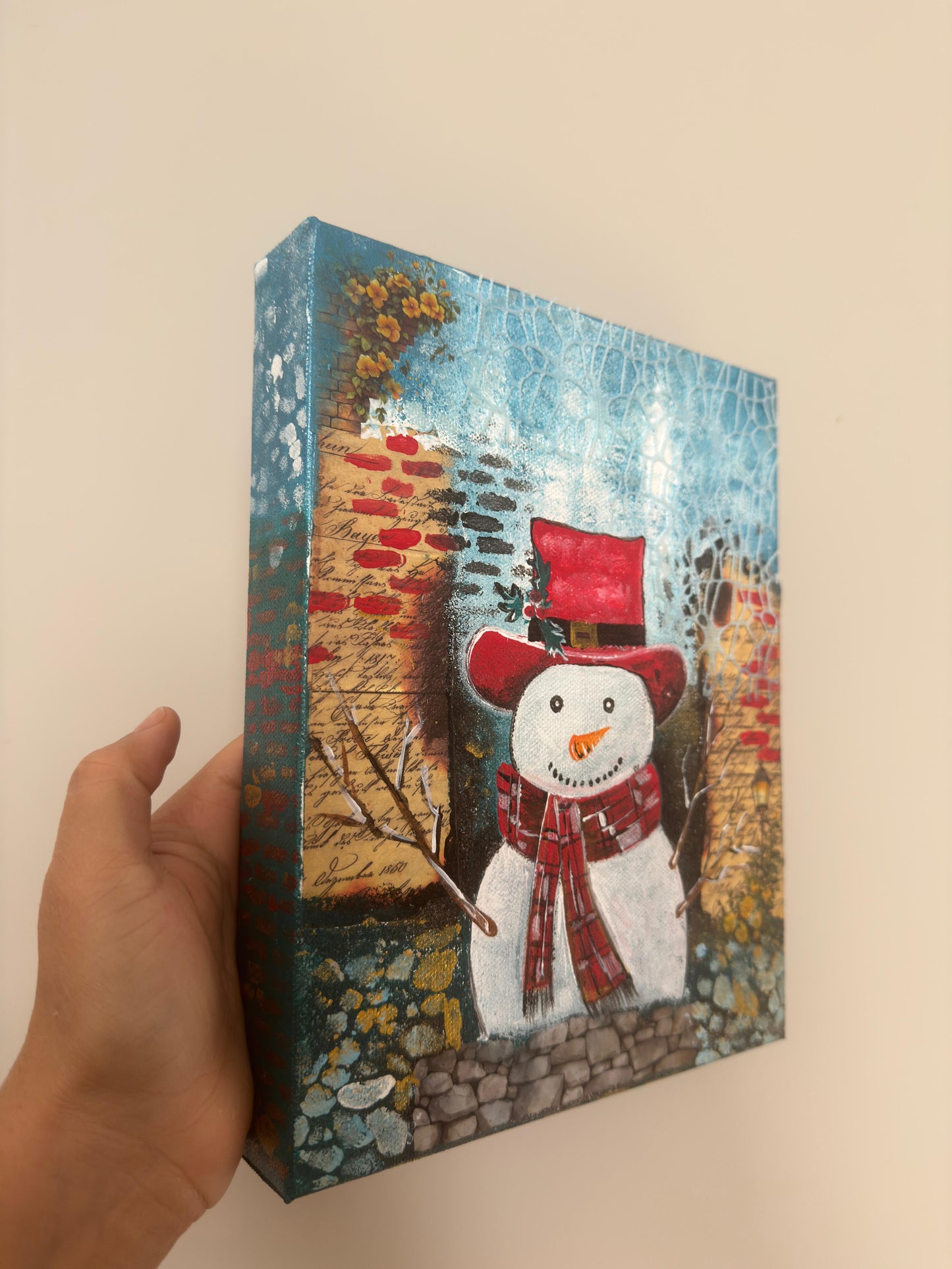Handmade acrylic painting of a snowman wearing a red hat and scarf with a textured winter brick background.