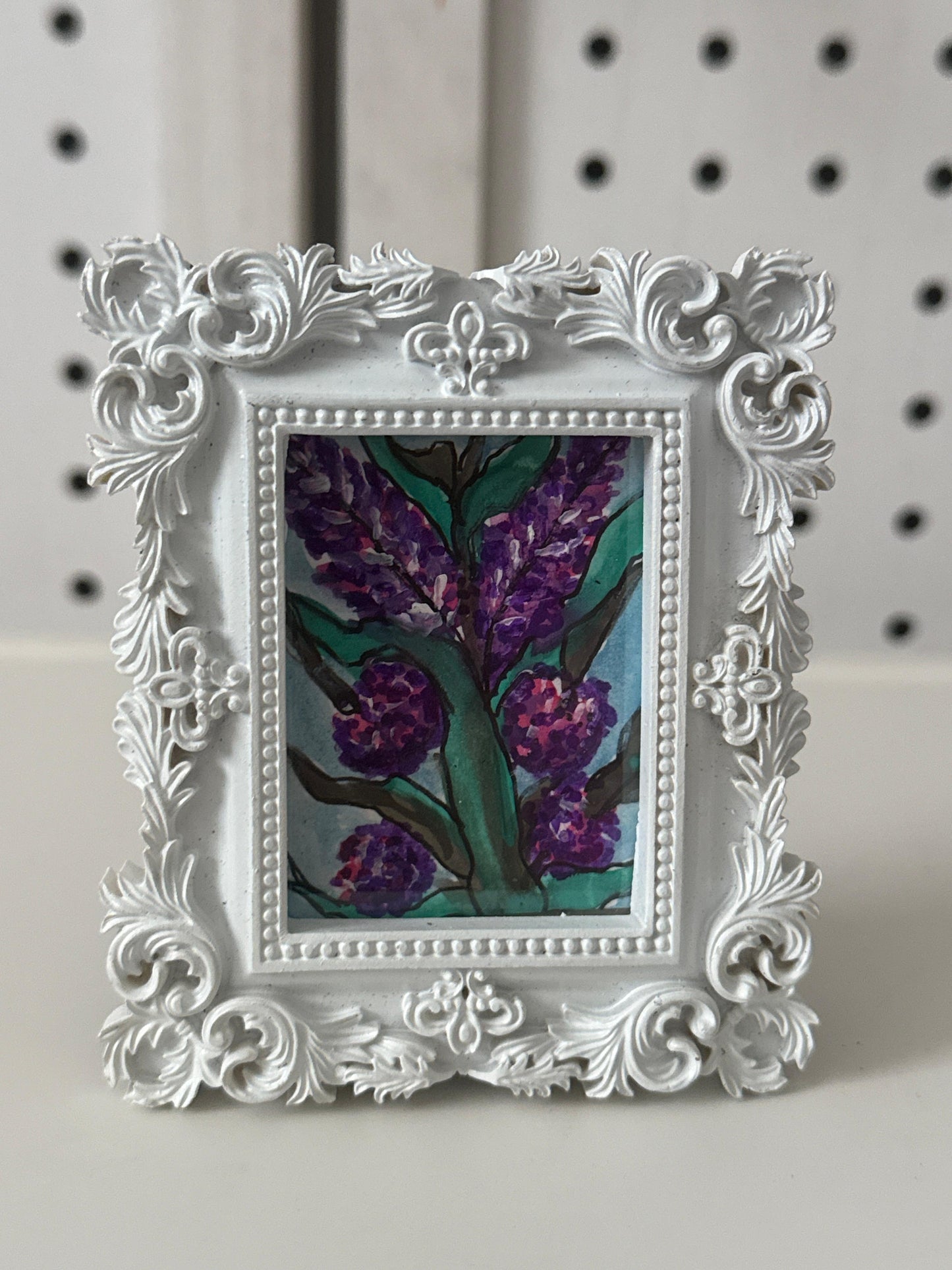 Decorative white frame with a floral painting on a pegboard background