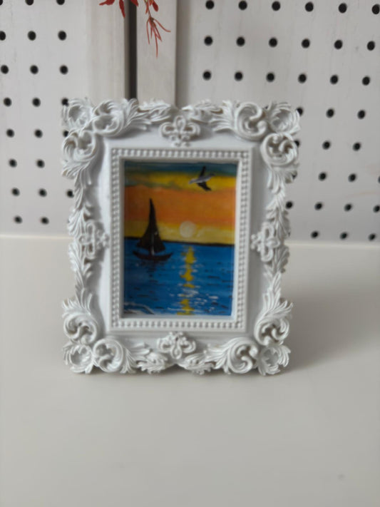 Decorative white frame with a small painting of a sailboat on a sunset background.