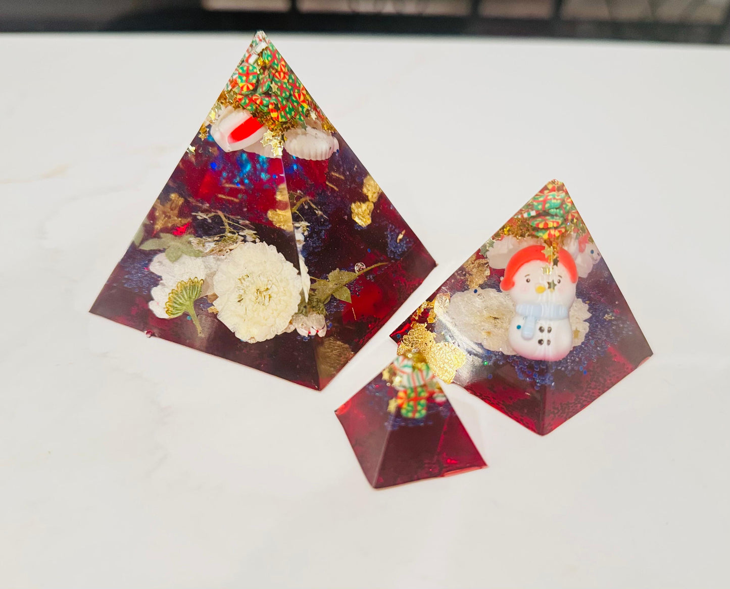 Two pyramid-shaped decorative items with floral and snowman designs on a white surface.