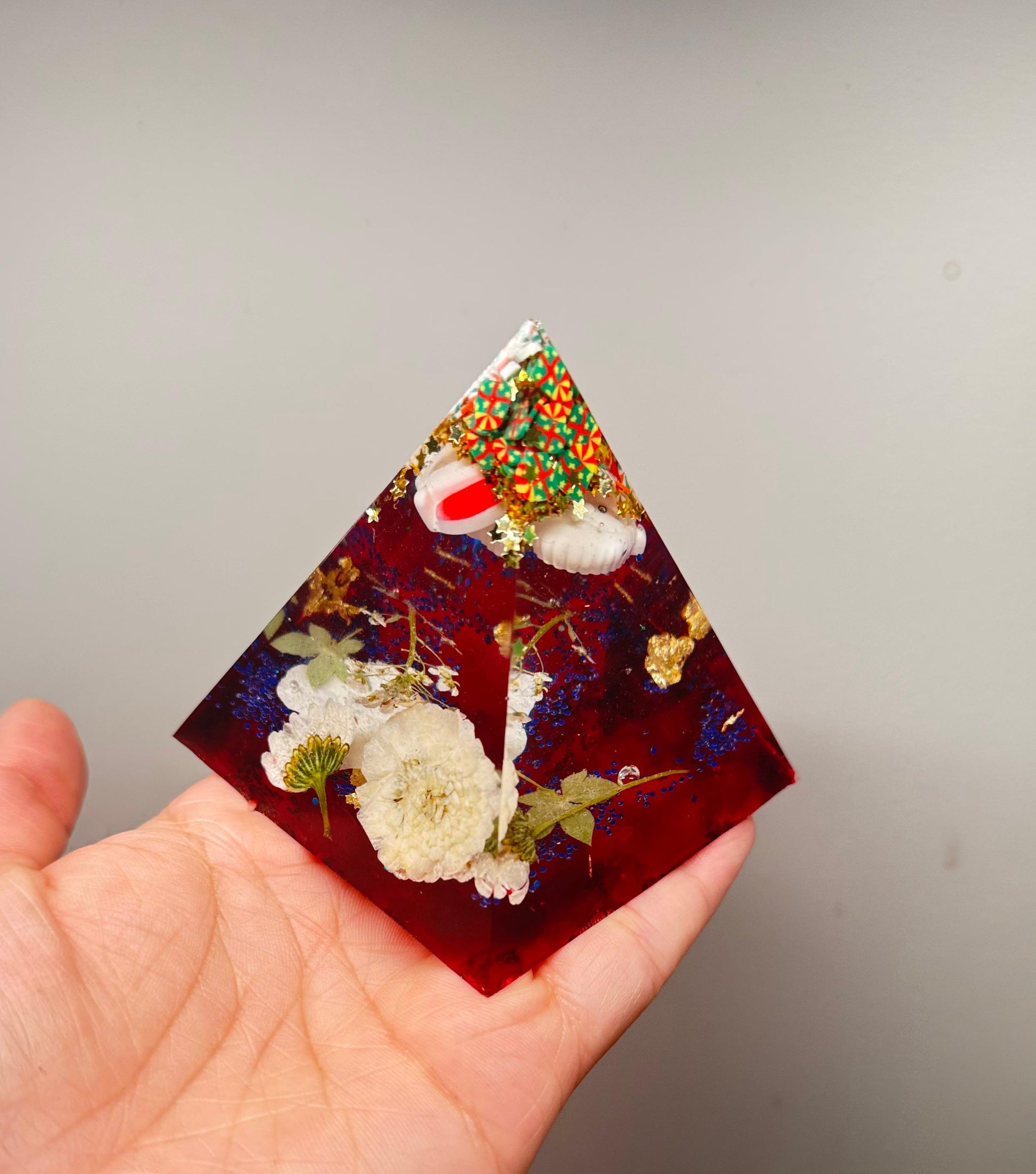 Triangular resin piece with embedded flowers and decorative elements held in a hand against a plain background
