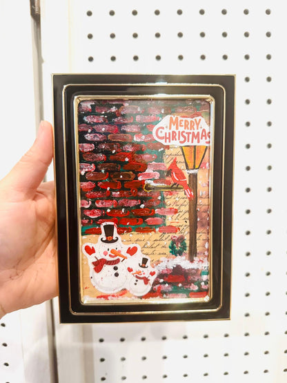 Framed Christmas painting with snowmen and festive design.