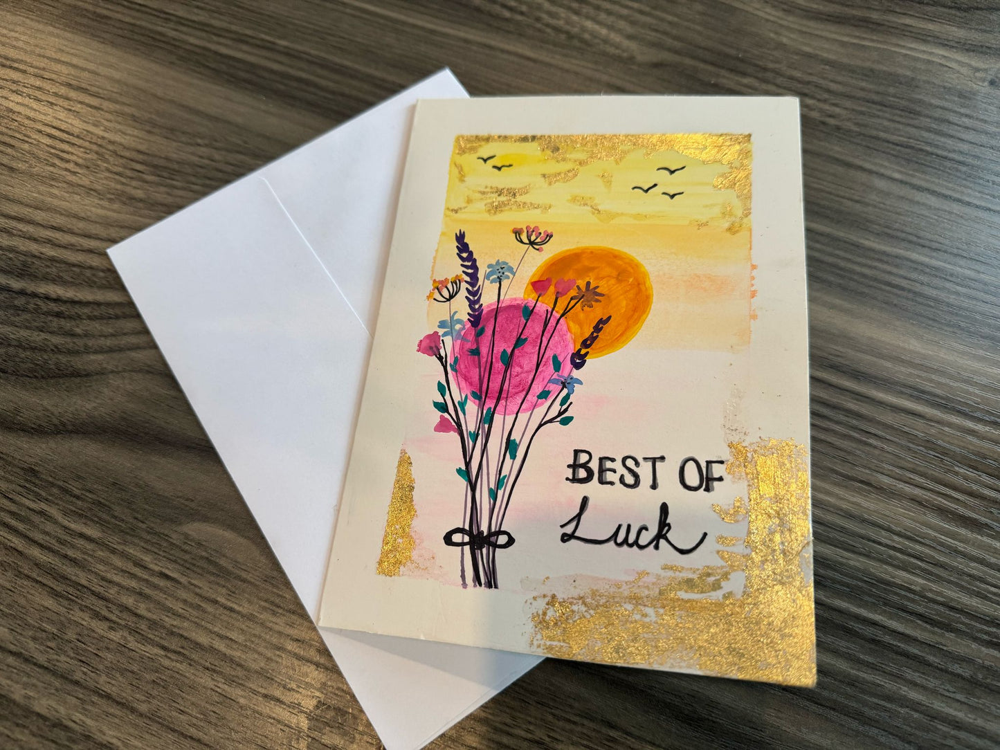Greeting card with floral design and 'Best of Luck' text on a wooden surface