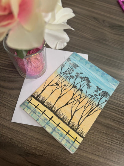 Hand-painted greeting card with tree silhouettes against a golden sunset sky – blank inside with envelope.