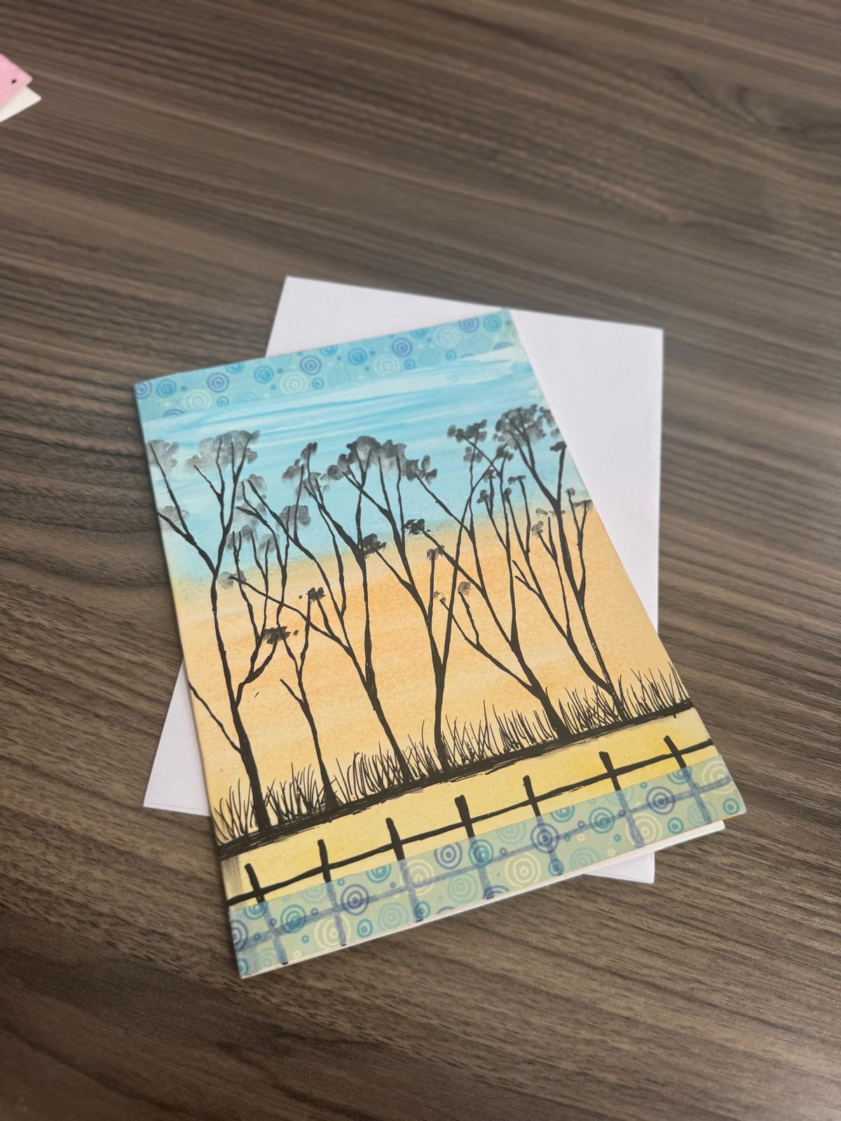 Hand-painted greeting card with tree silhouettes against a golden sunset sky – blank inside with envelope.